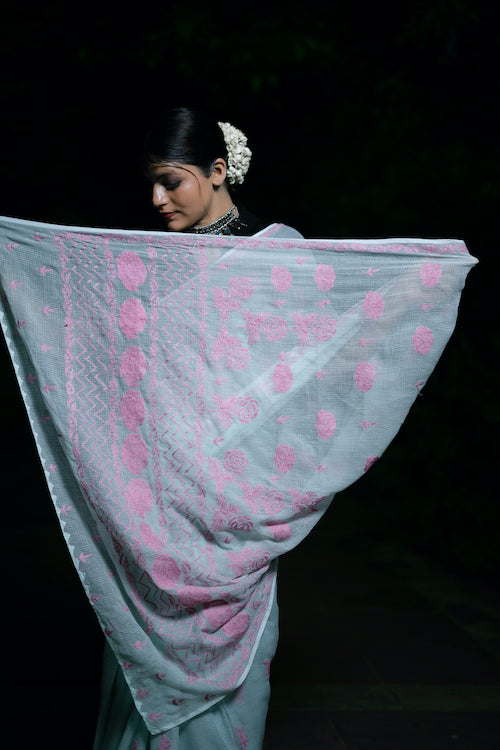 Woman holding a light blue saree with pink patterns against a dark background