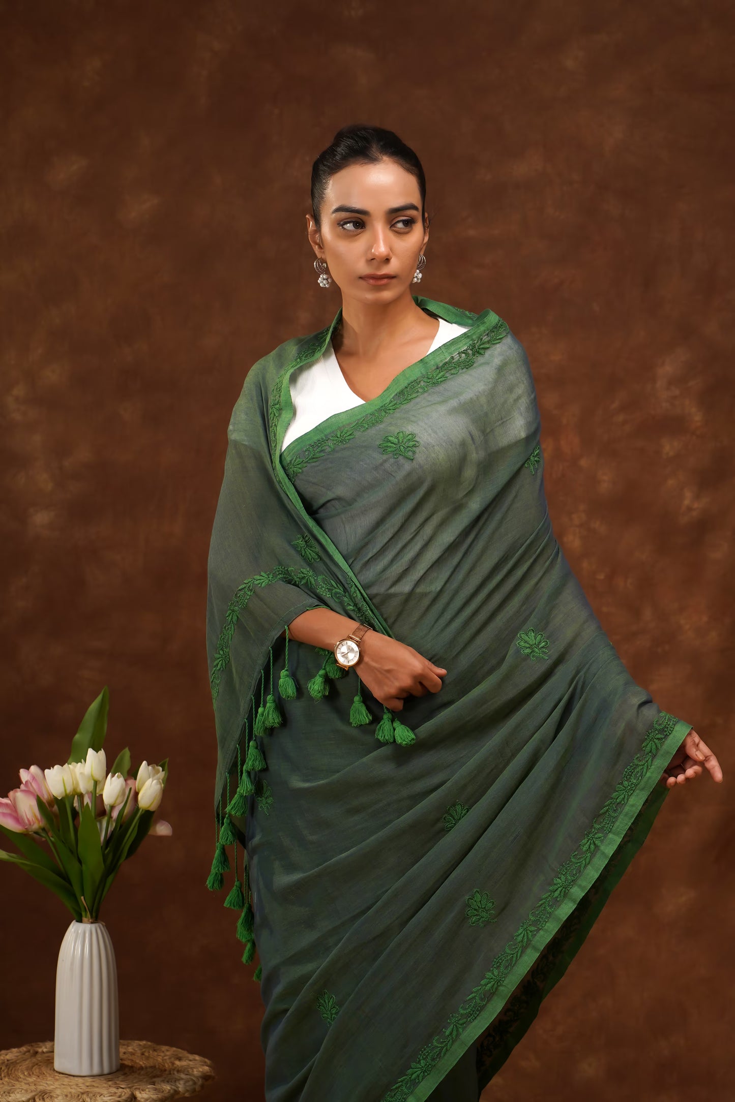 Woman wearing a dark green saree with a brown background.