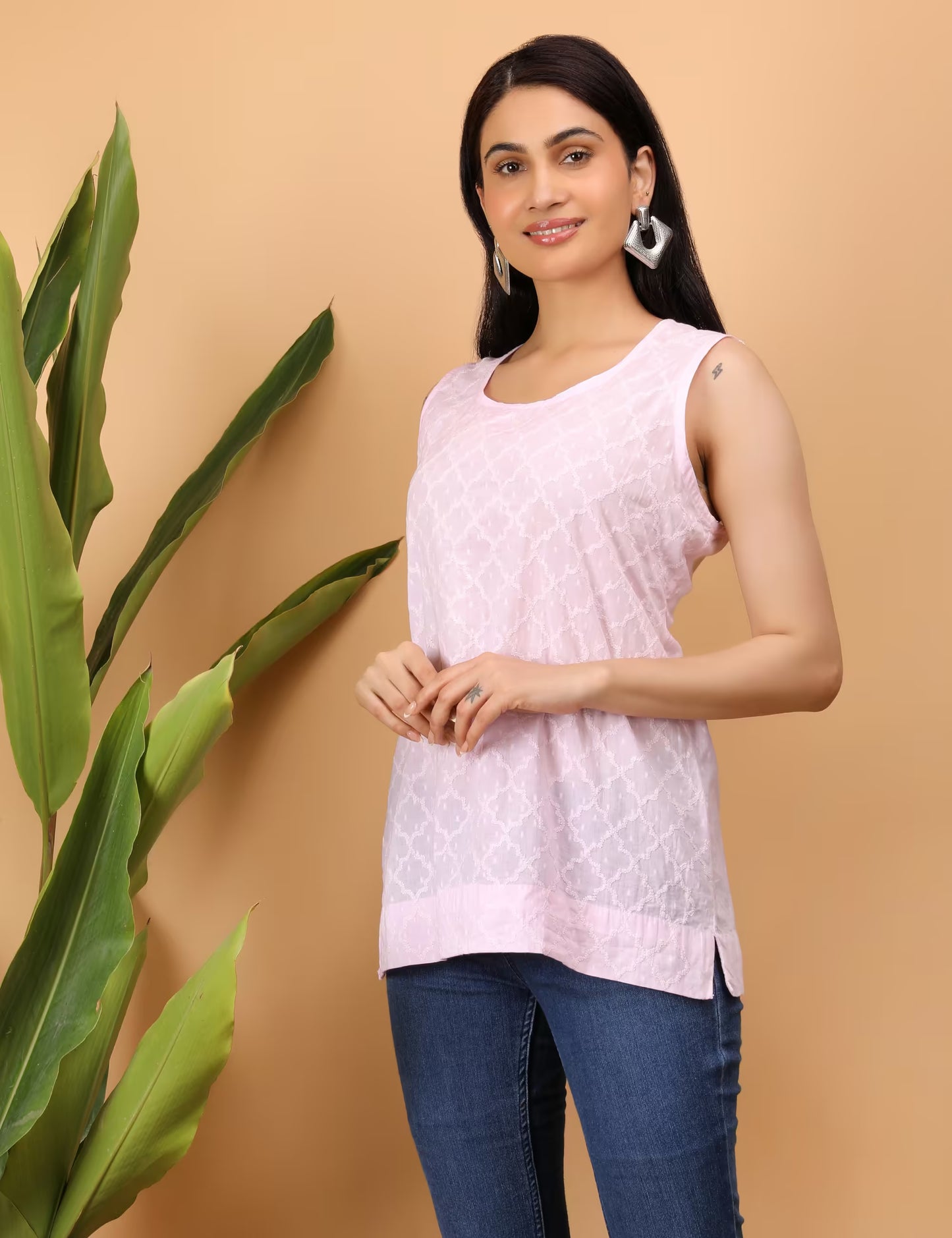 Woman wearing a light pink Chikankari sleeveless top with a plant on a beige background