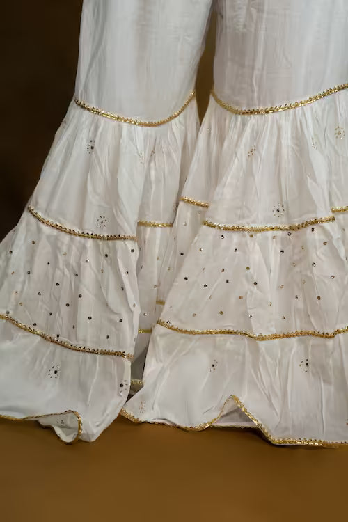 Close-up of a white Chikankari fabric with gold trim on a brown background