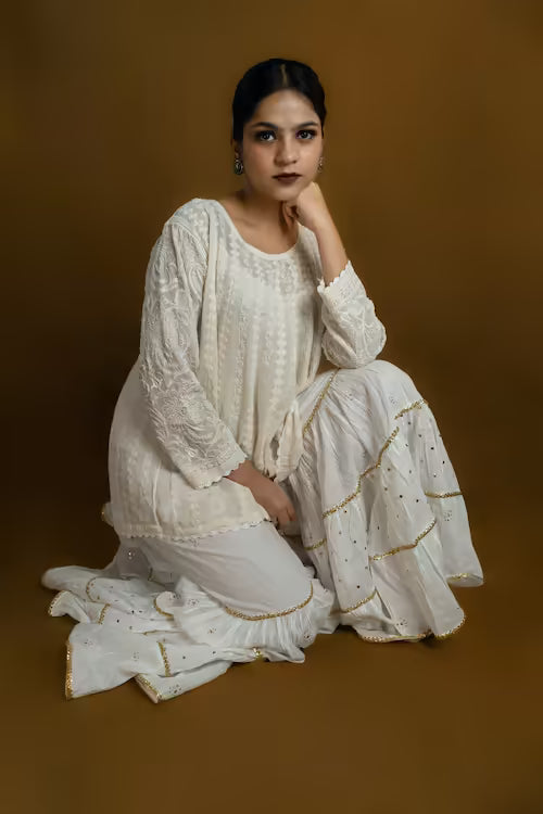 Woman in a white Chikankari traditional outfit with gold details on a brown background