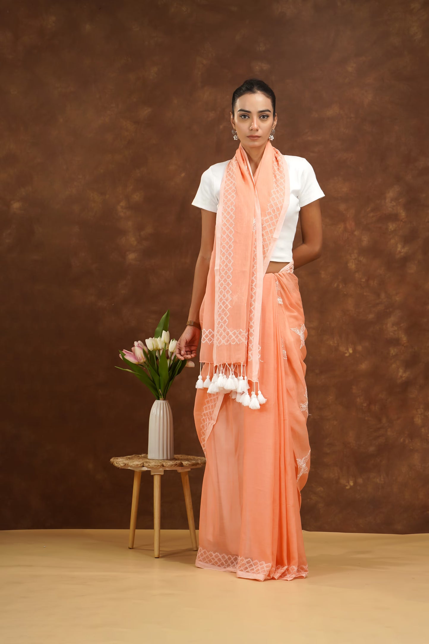 Woman in peach saree with white blouse against a brown background