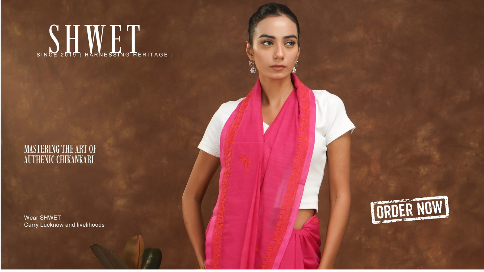Woman wearing a pink saree with a brown background, featuring the brand 'SHWET'.