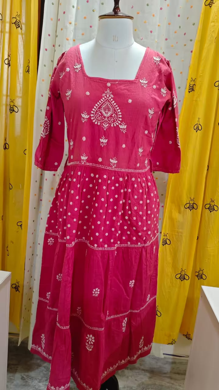 Pink dress with white Chikankari patterns on a mannequin against a yellow curtain background
