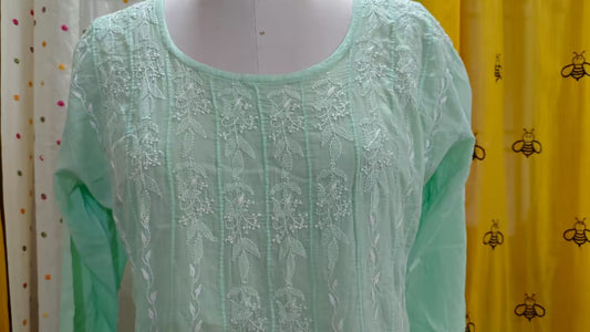 Light green Chikankari top on a mannequin with colorful curtains in the background