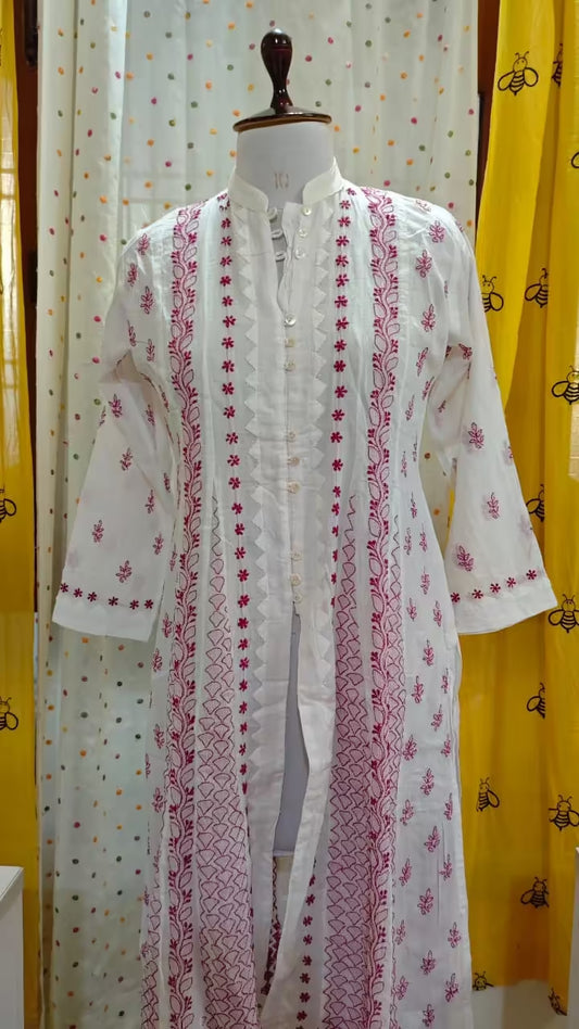 White embroidered kurta with pink Chikankari patterns on a mannequin against a yellow curtain background