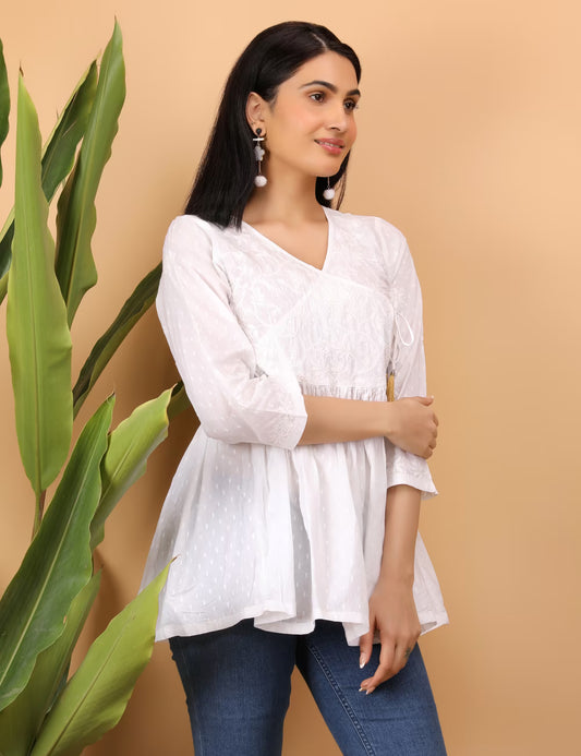 Woman wearing a white hand embroidered chikankari top with blue jeans against a beige background