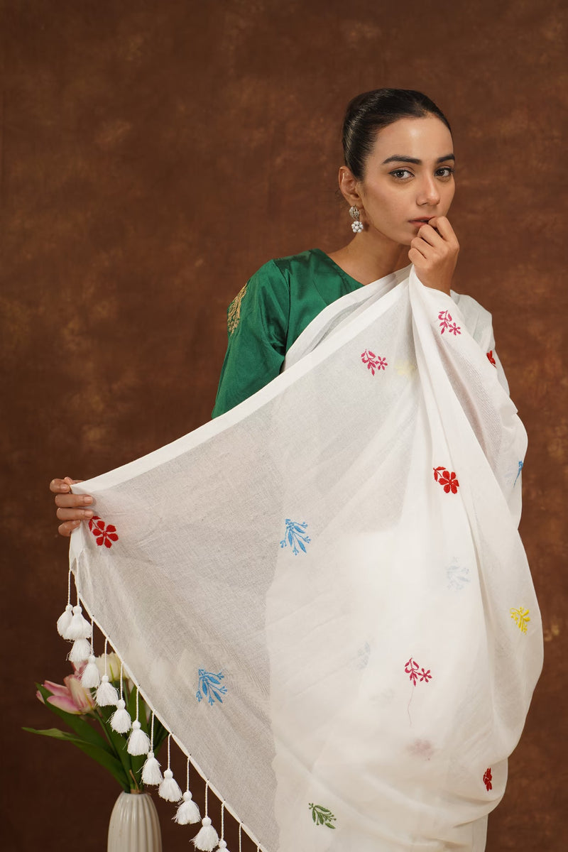 A model is wearing a handmade chikankari white saree against a brown backdrop. 