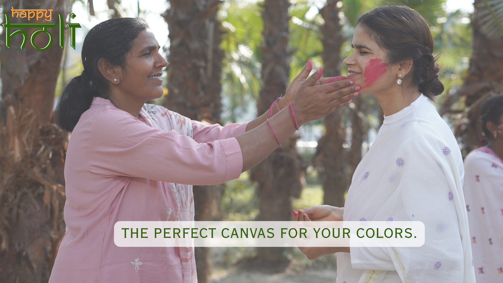 Two women applying traditional makeup with a natural outdoor setting and 'Happy Holi' text.
