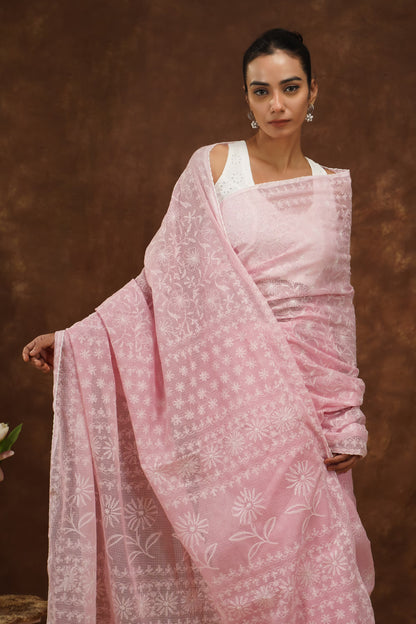 Woman wearing a baby pink saree with white patterns against a brown background.