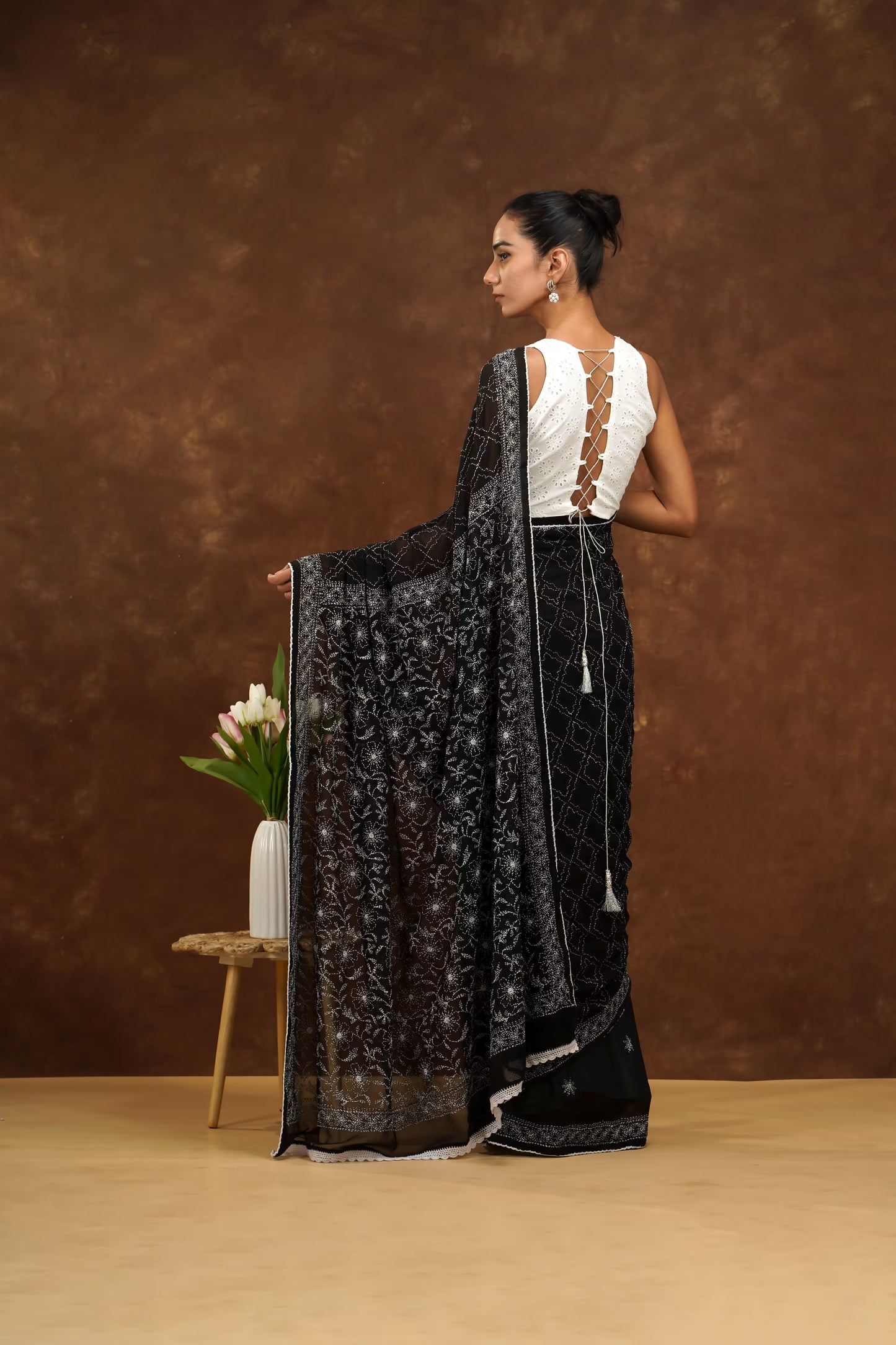 Woman holding a black saree with a white blouse against a brown background