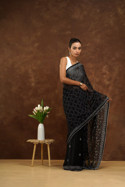 Woman in a black saree with white blouse against a brown background