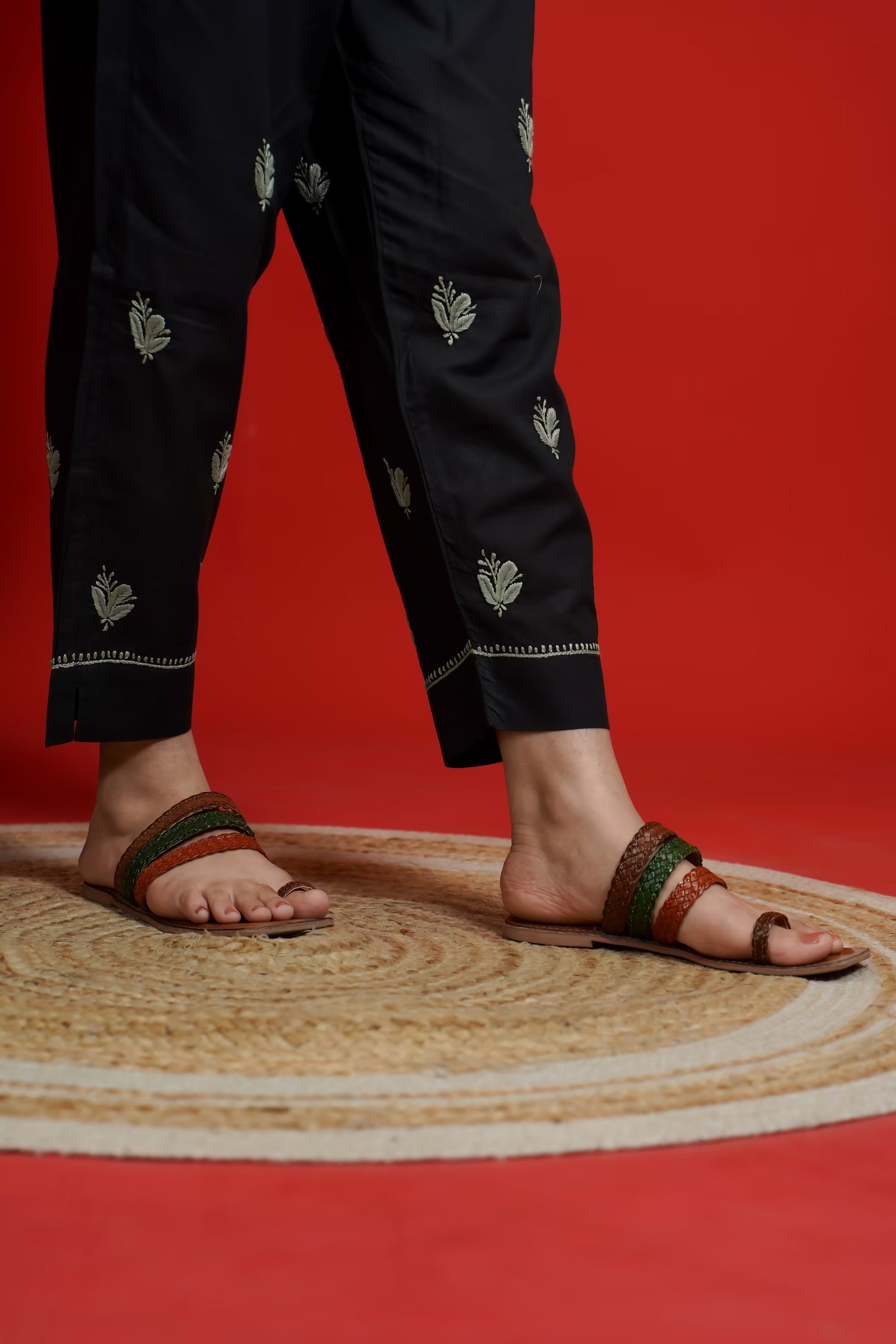 Person wearing black pants with green patterns and sandals on a red background