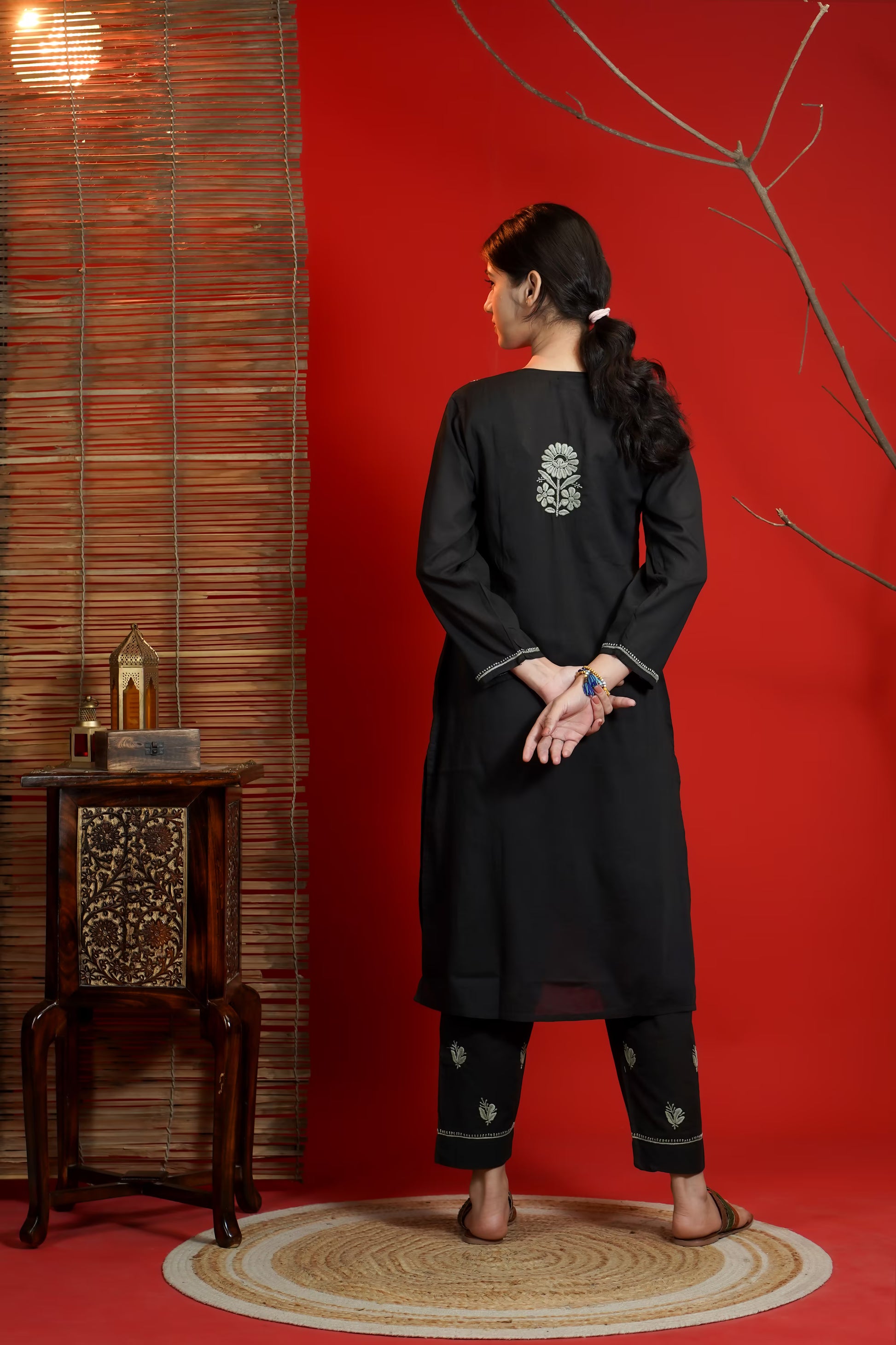 Woman wearing a black kurta with white patterns in a room with red walls and wooden furniture.