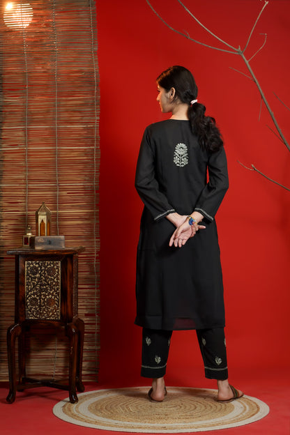 Woman wearing a black kurta with white patterns in a room with red walls and wooden furniture.