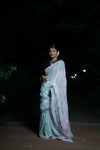 Woman in a light blue saree with pink patterns standing outdoors at night.