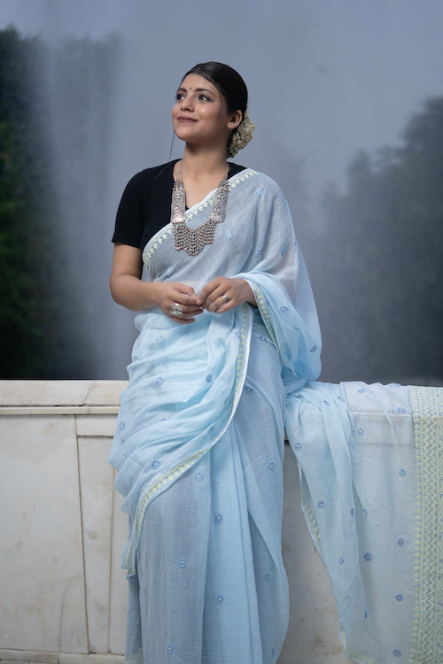 Woman in a light blue saree with a blurred fountain background