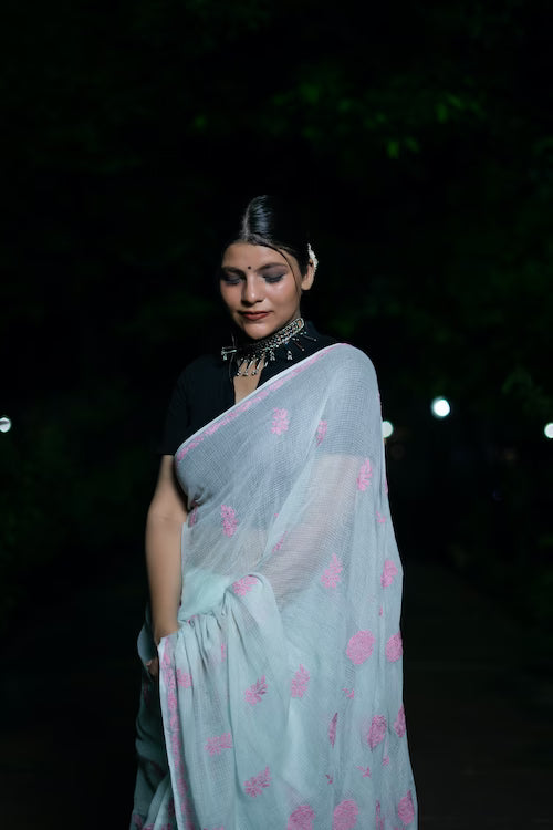 Woman wearing a light blue saree with pink patterns at night.