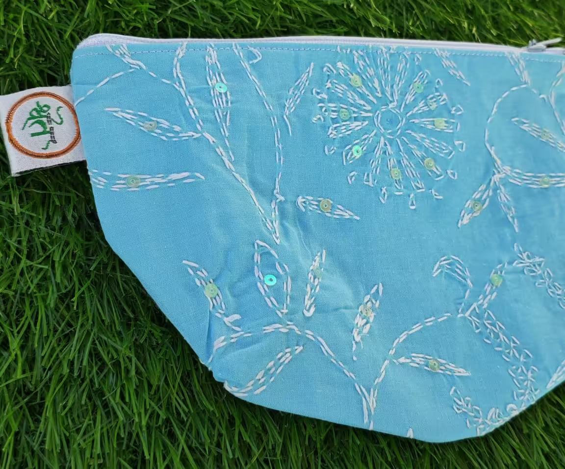 Blue fPouch with white floral Chikankari pattern on a grass background