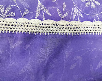Chikankari Close-up of white lace trim on a purple fabric background with floral patterns.