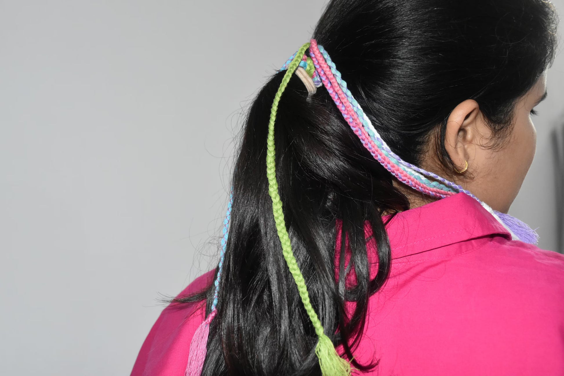 Person with colorful braided hair tie and pink shirt on a plain background