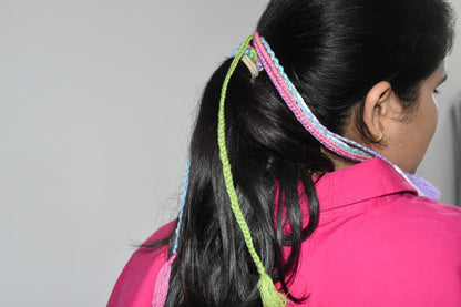 Person with colorful braided hair tie and pink shirt on a plain background