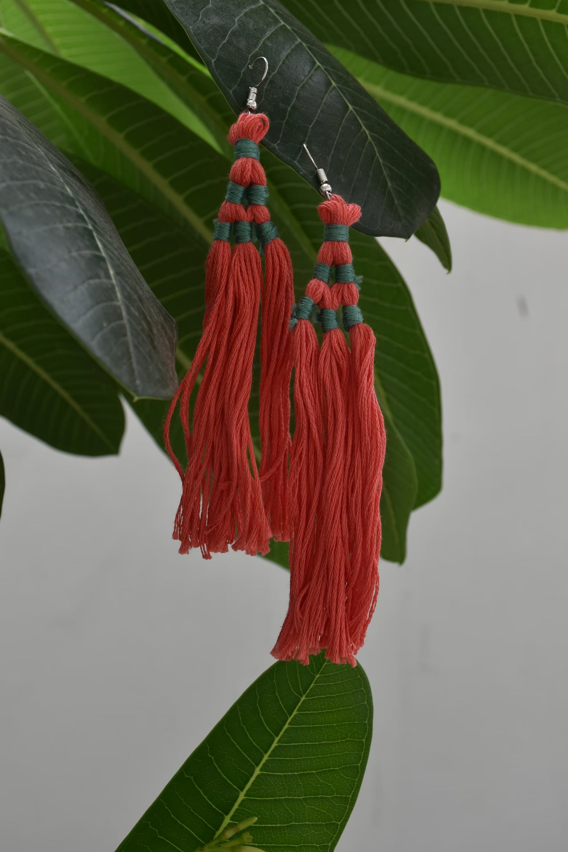 Red tassel earrings with green accents on a leafy background