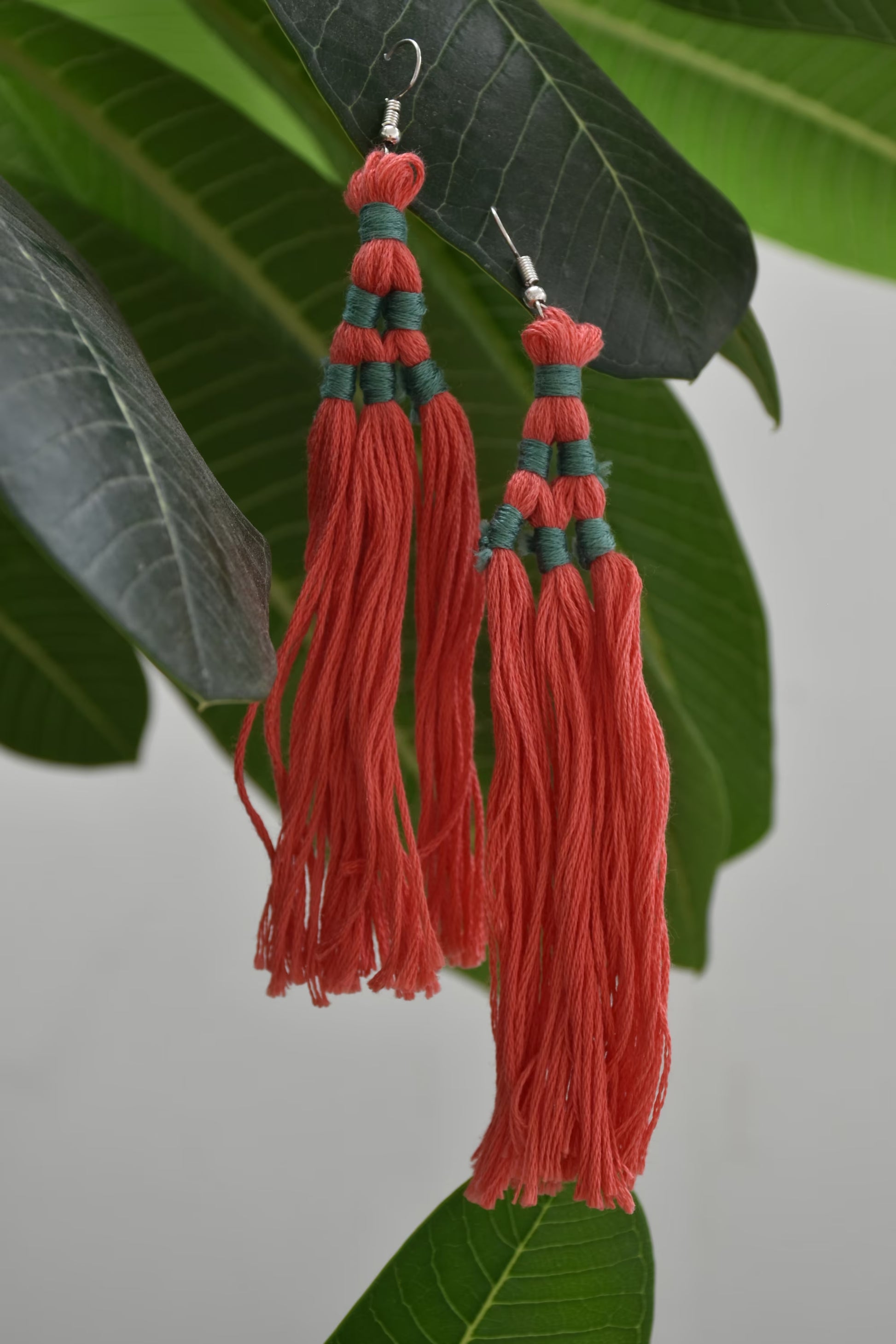 Red tassel earrings with green accents on a leaf background