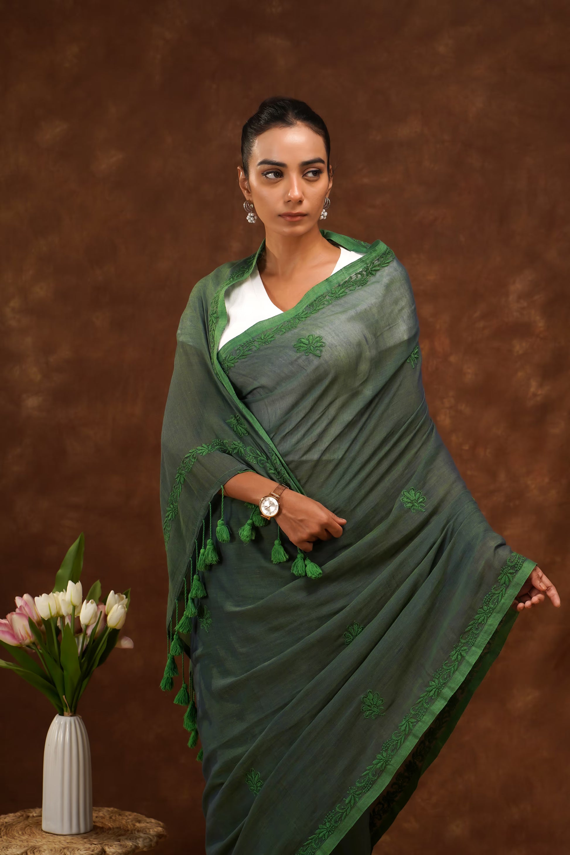 Woman wearing a dark green saree with a brown background.