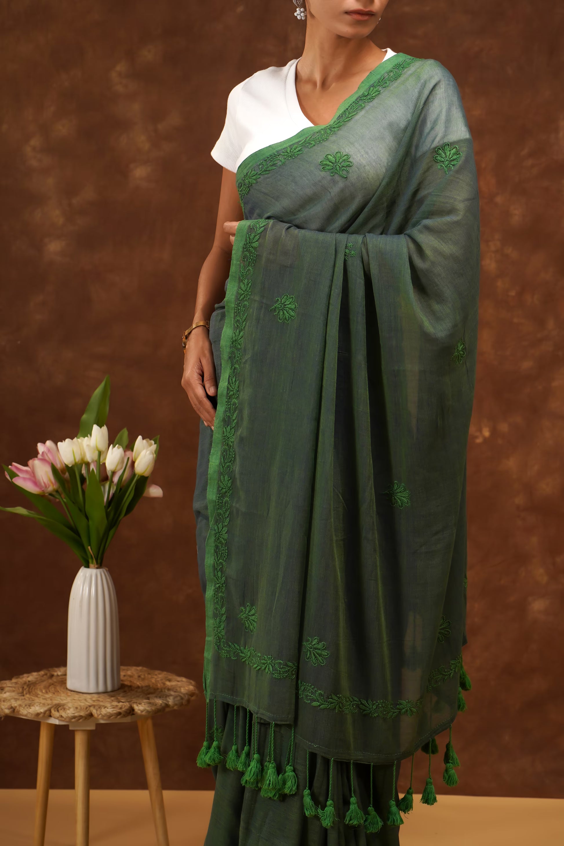 Woman wearing a dark green saree with white blouse against a brown background