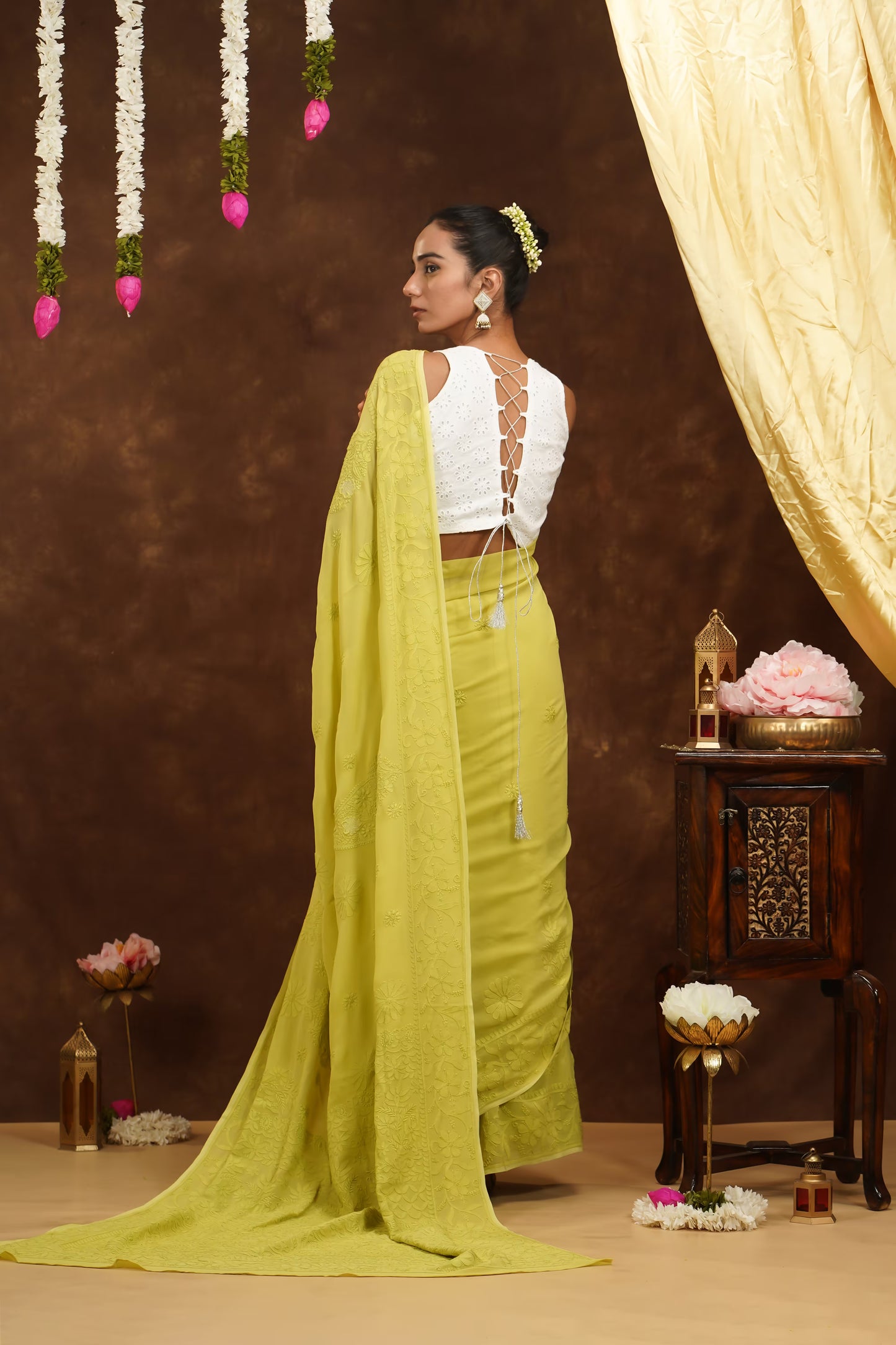 Woman in a yellow saree with a white blouse against a decorated backdrop