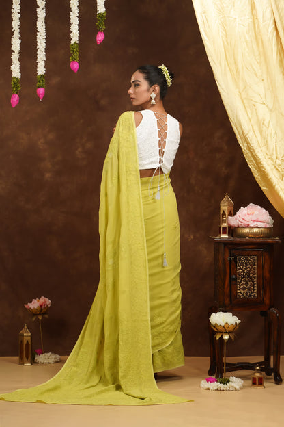 Woman in a yellow saree with a white blouse against a decorated backdrop