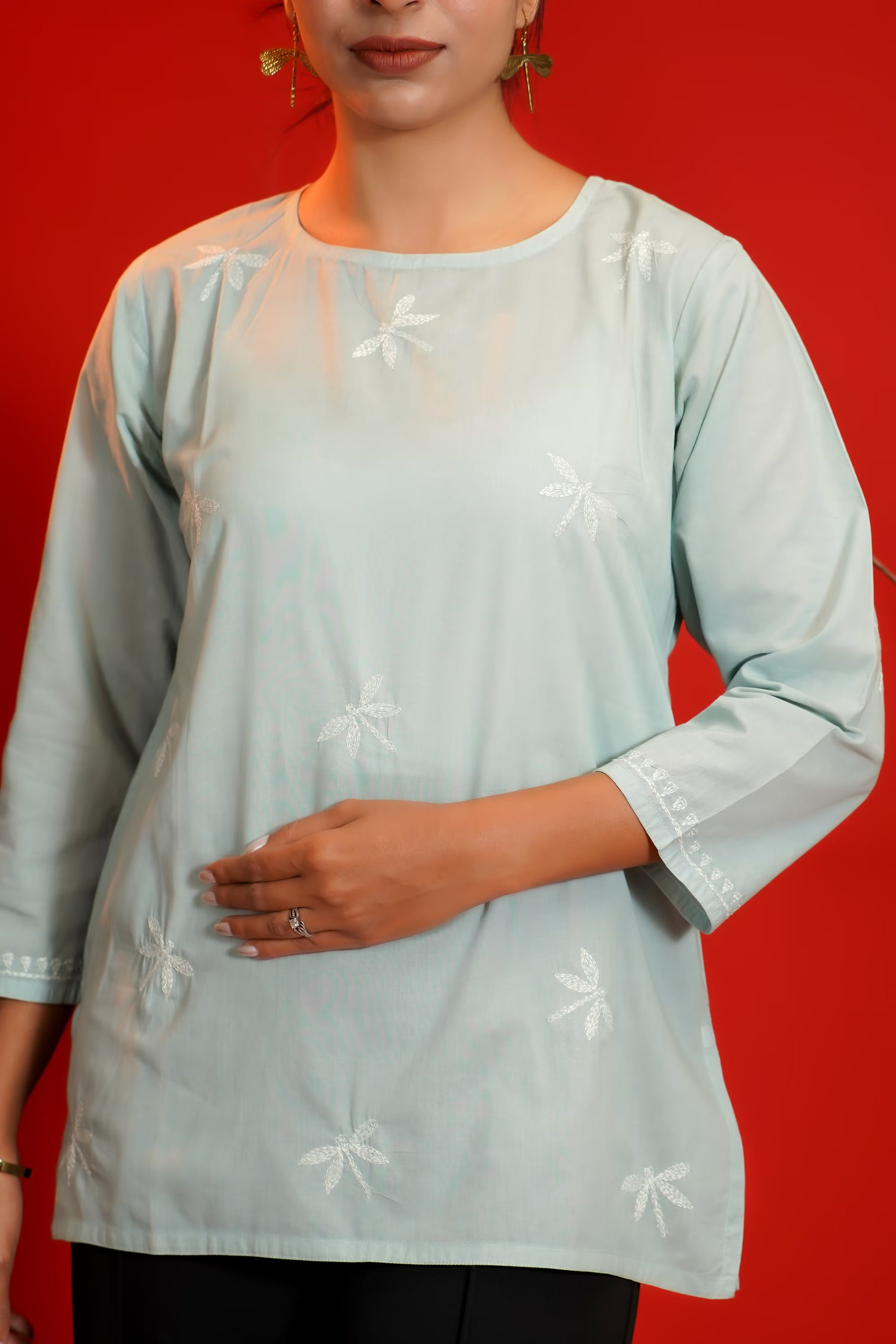 Grey embroidered top worn by a person on a red background