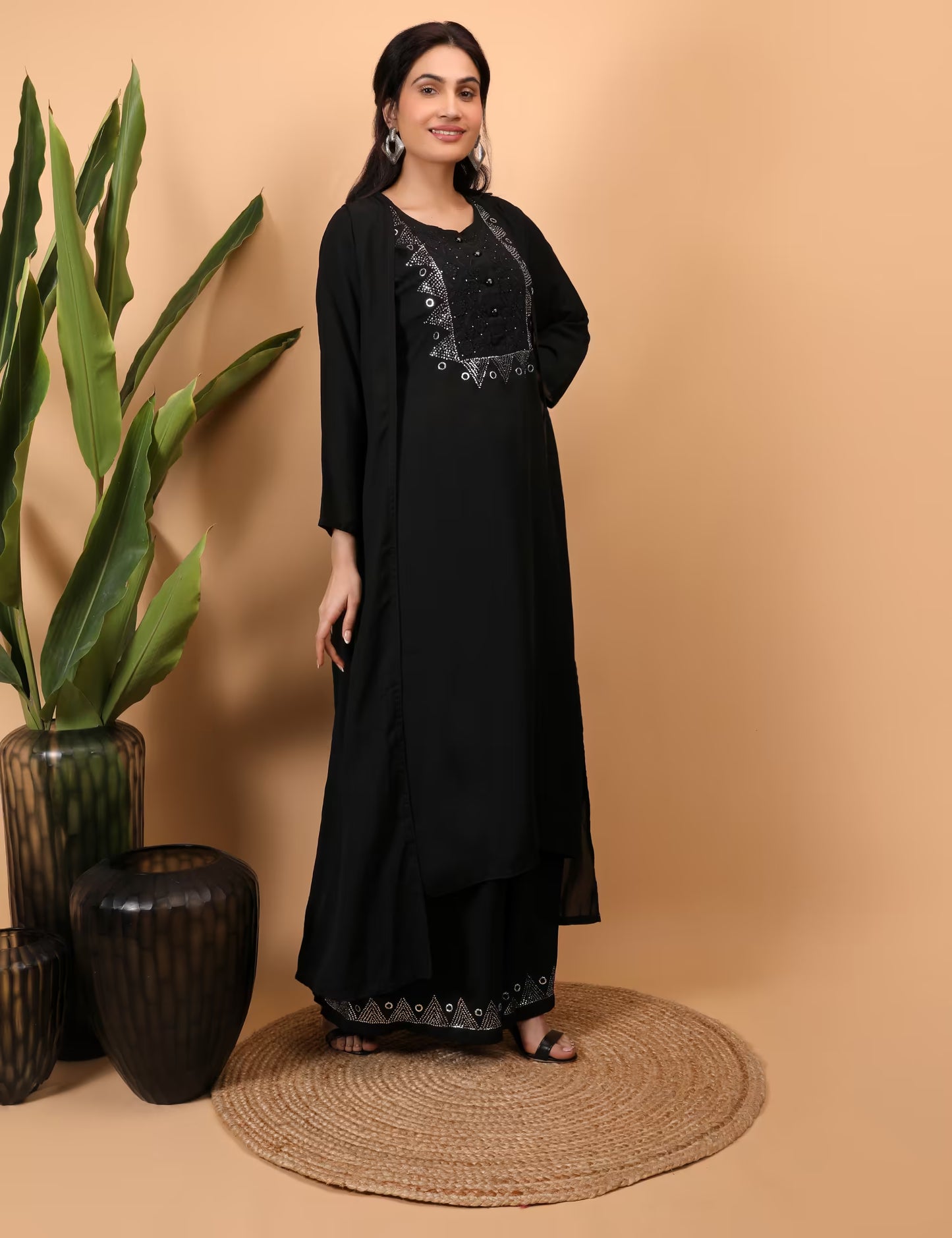 Woman wearing a black Kurti Plazzo Shrug Set with embroidery standing next to decorative vases on a beige background