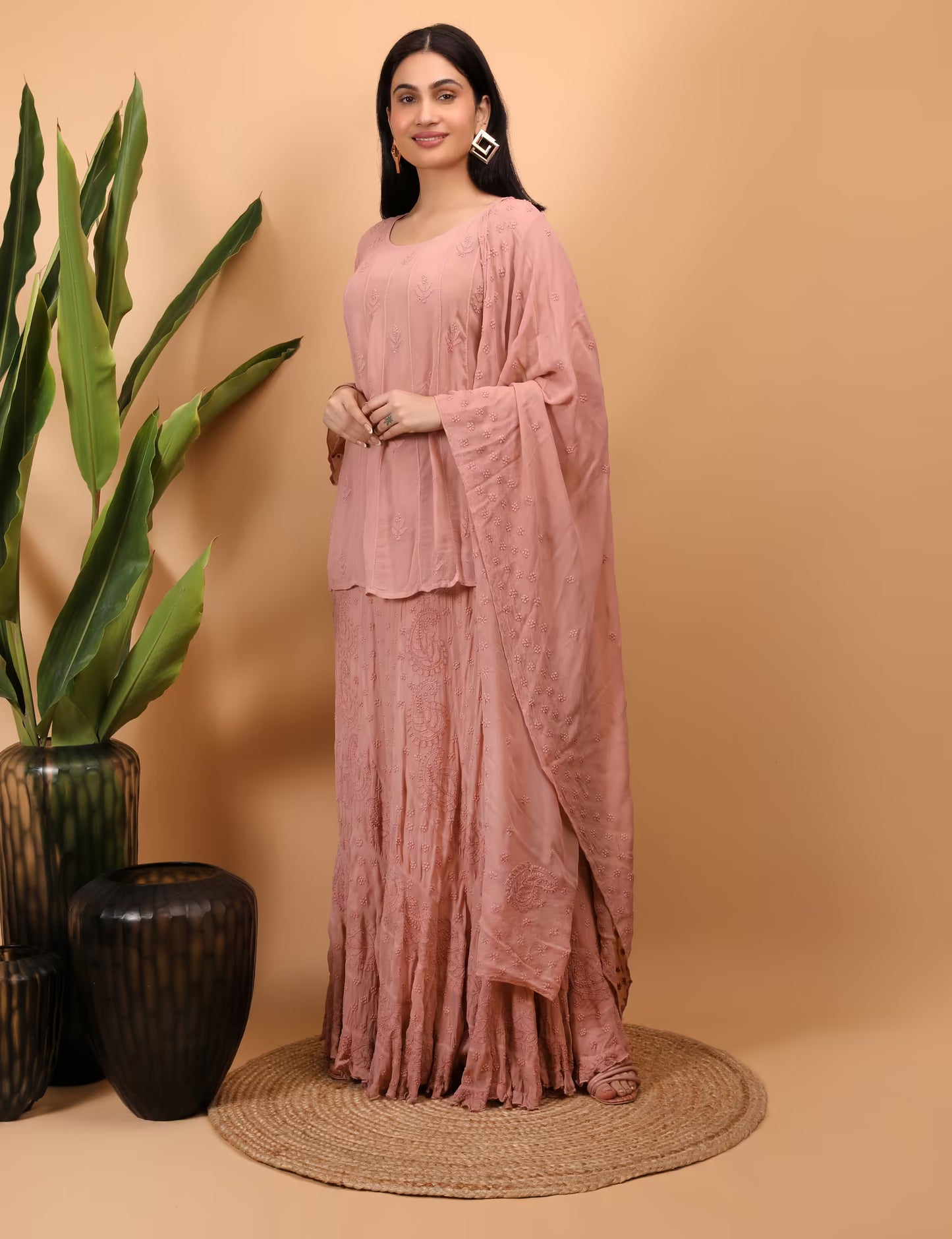 Woman in a peach Lahenga Set standing next to decorative vases on a beige background
