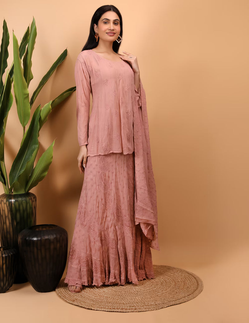 Woman in a peach traditional outfit standing against a beige background with plants.