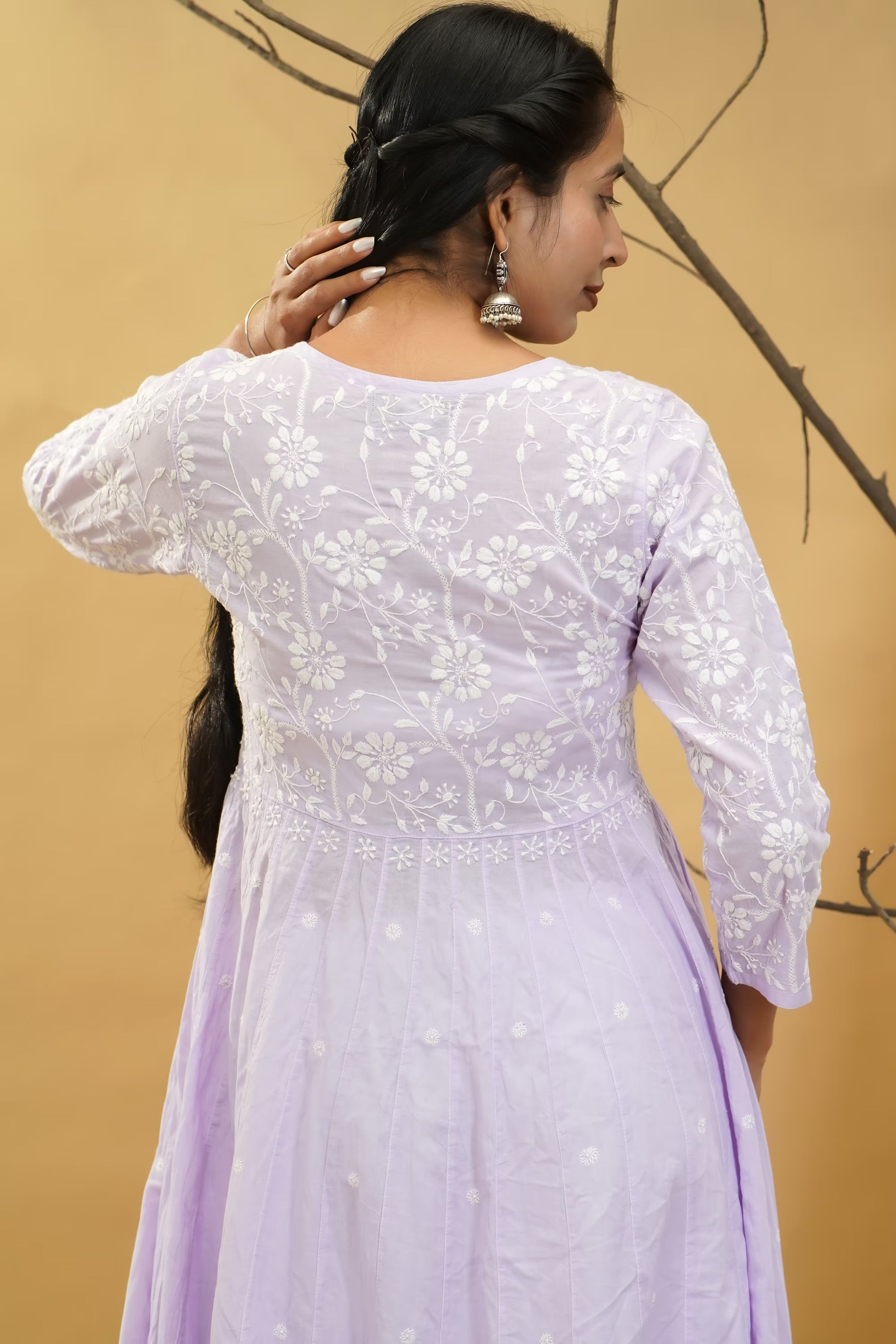 Woman wearing a light purple dress with floral embroidery against a beige background.