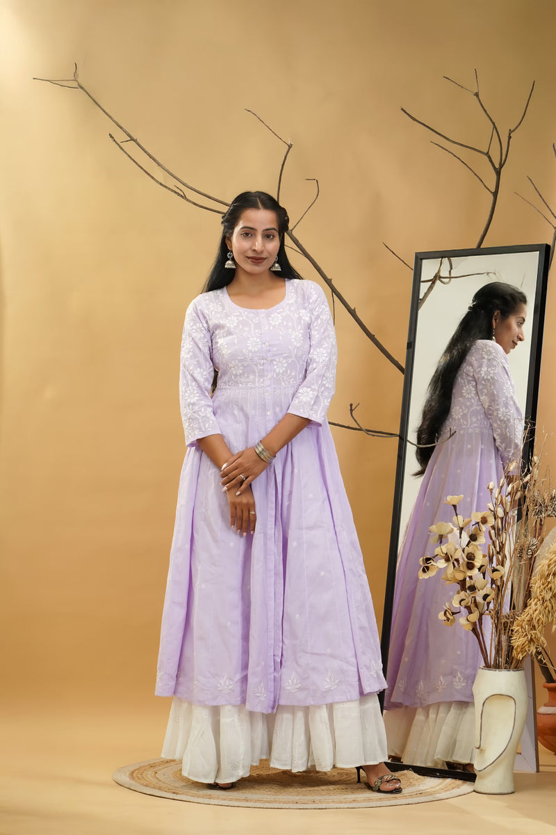 Woman in a light purple dress standing next to a mirror on a beige background