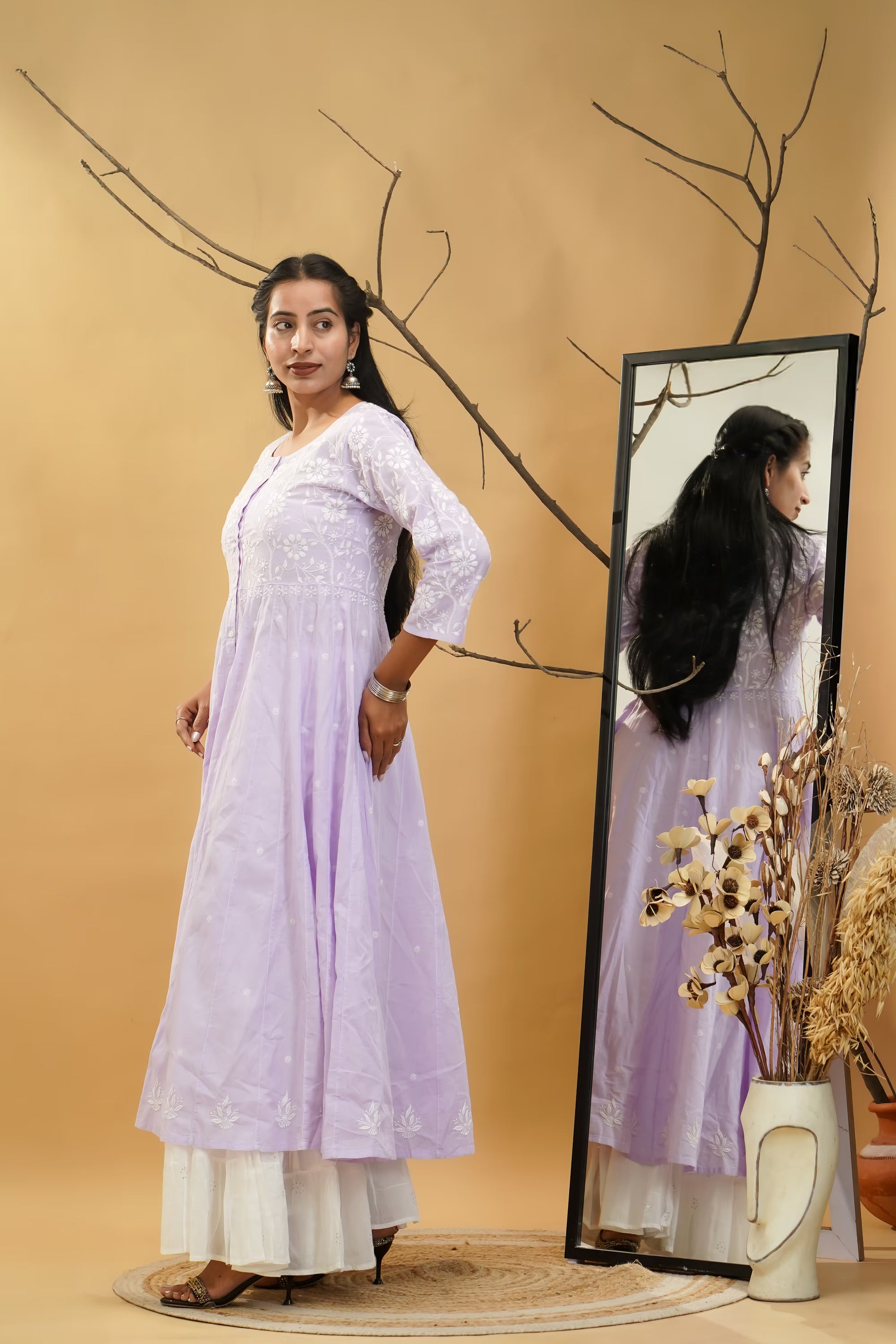 Woman in a light purple dress standing next to a mirror on a beige background