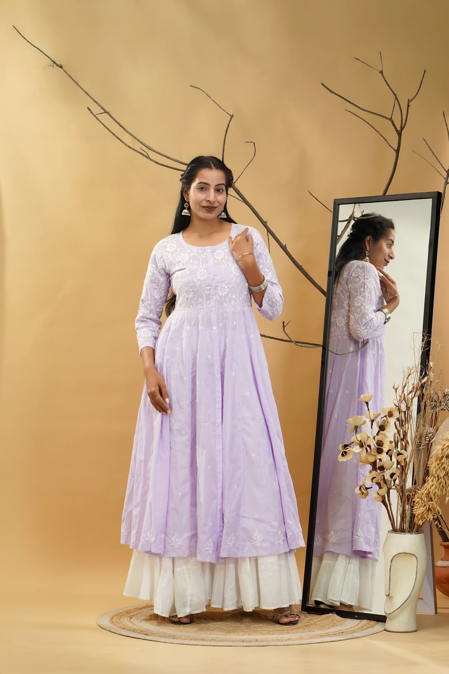 Woman in a light purple dress standing next to a mirror on a beige background