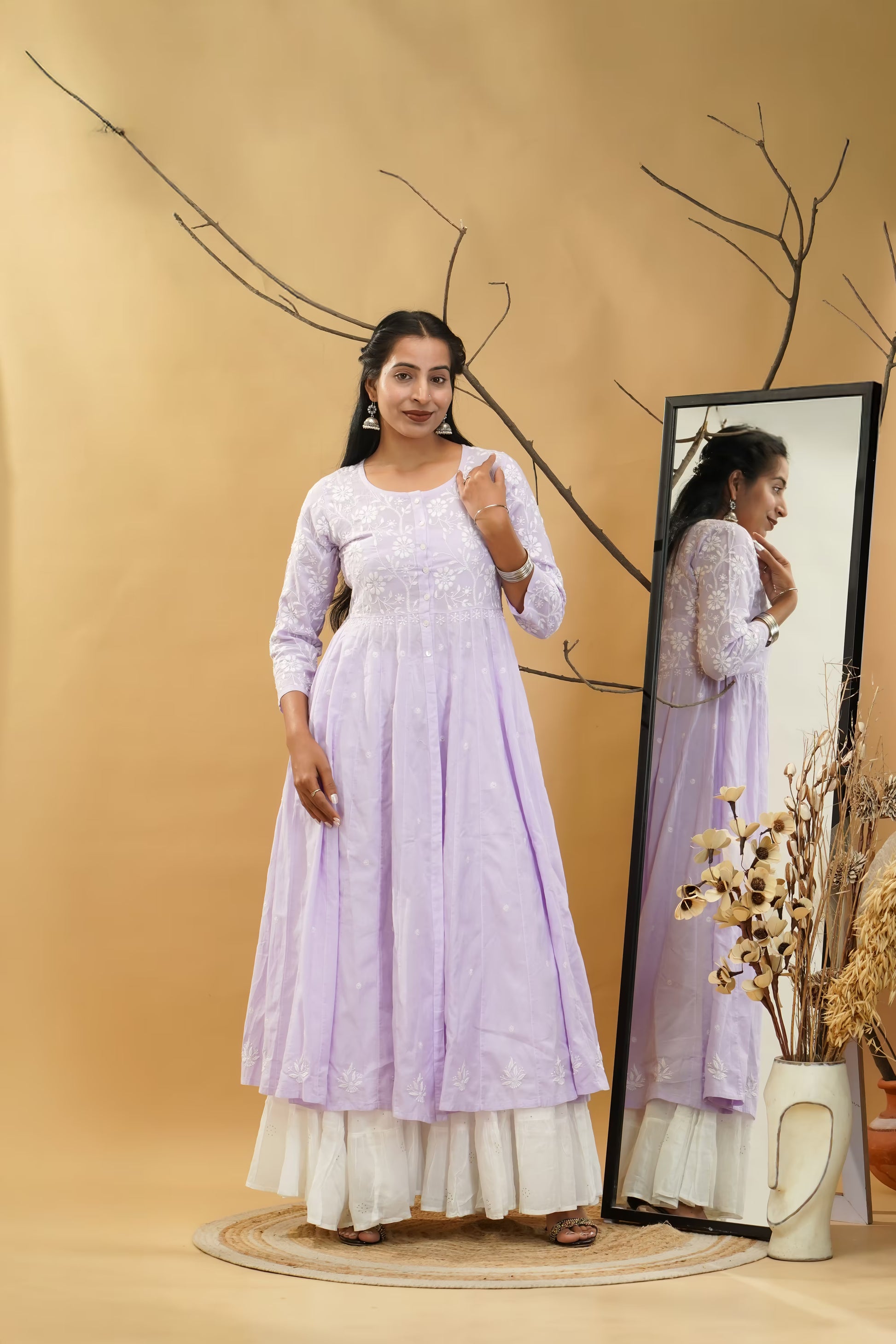 Woman in a light purple dress standing next to a mirror on a beige background