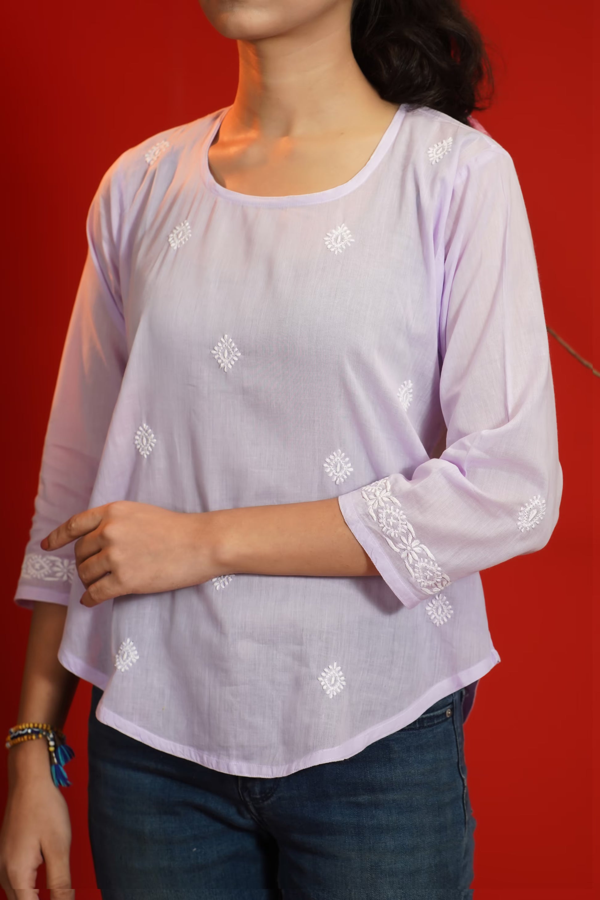 Lavender blouse with white floral embroidery worn by a person against a red background