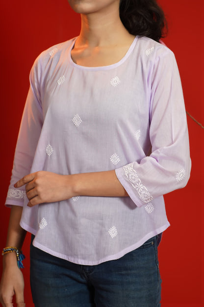 Lavender blouse with white floral embroidery worn by a person against a red background