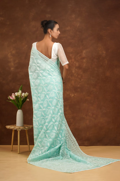 Woman wearing a light blue saree with a white blouse against a brown background