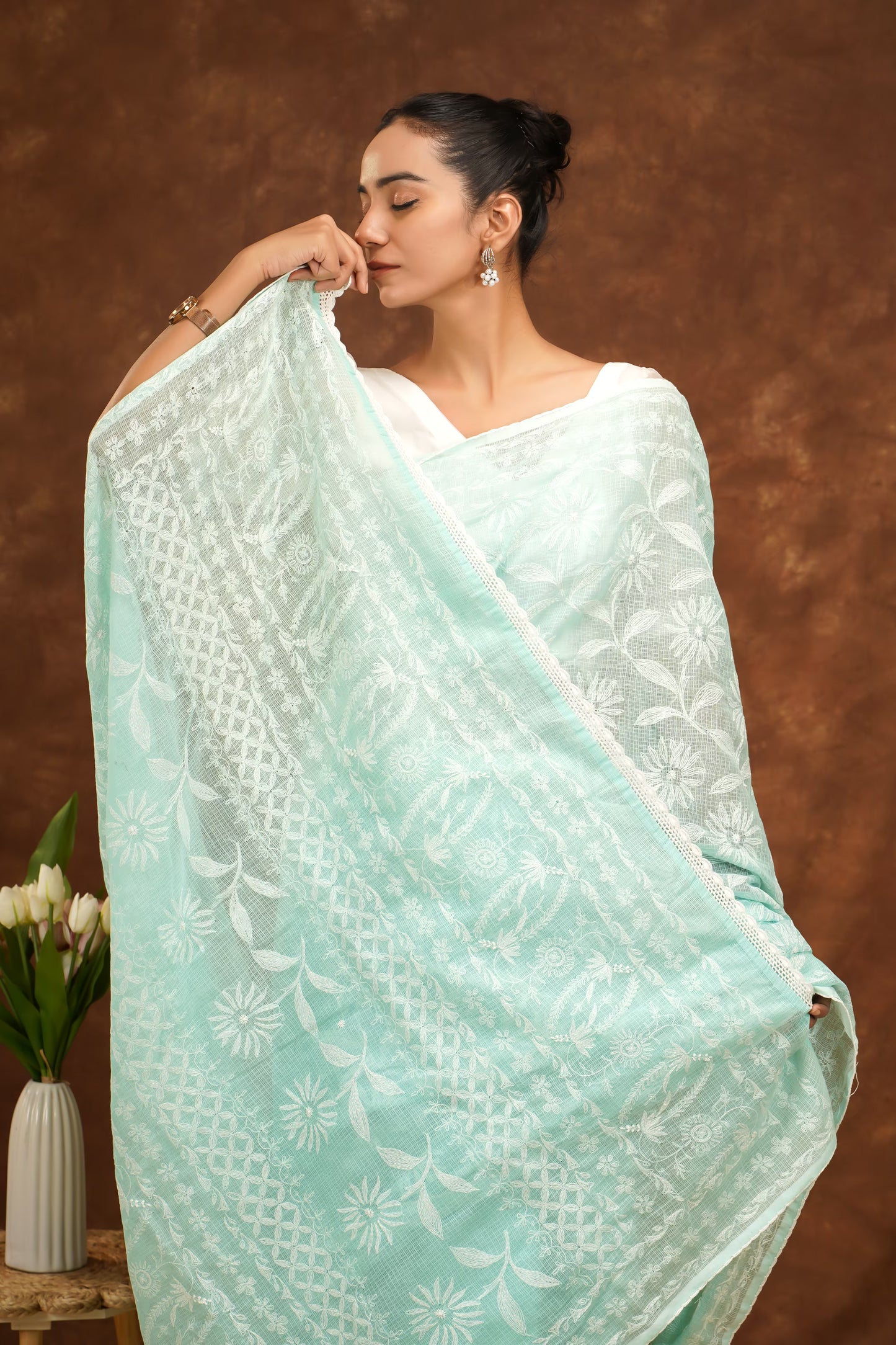 Woman wearing a light blue saree with white patterns against a brown background