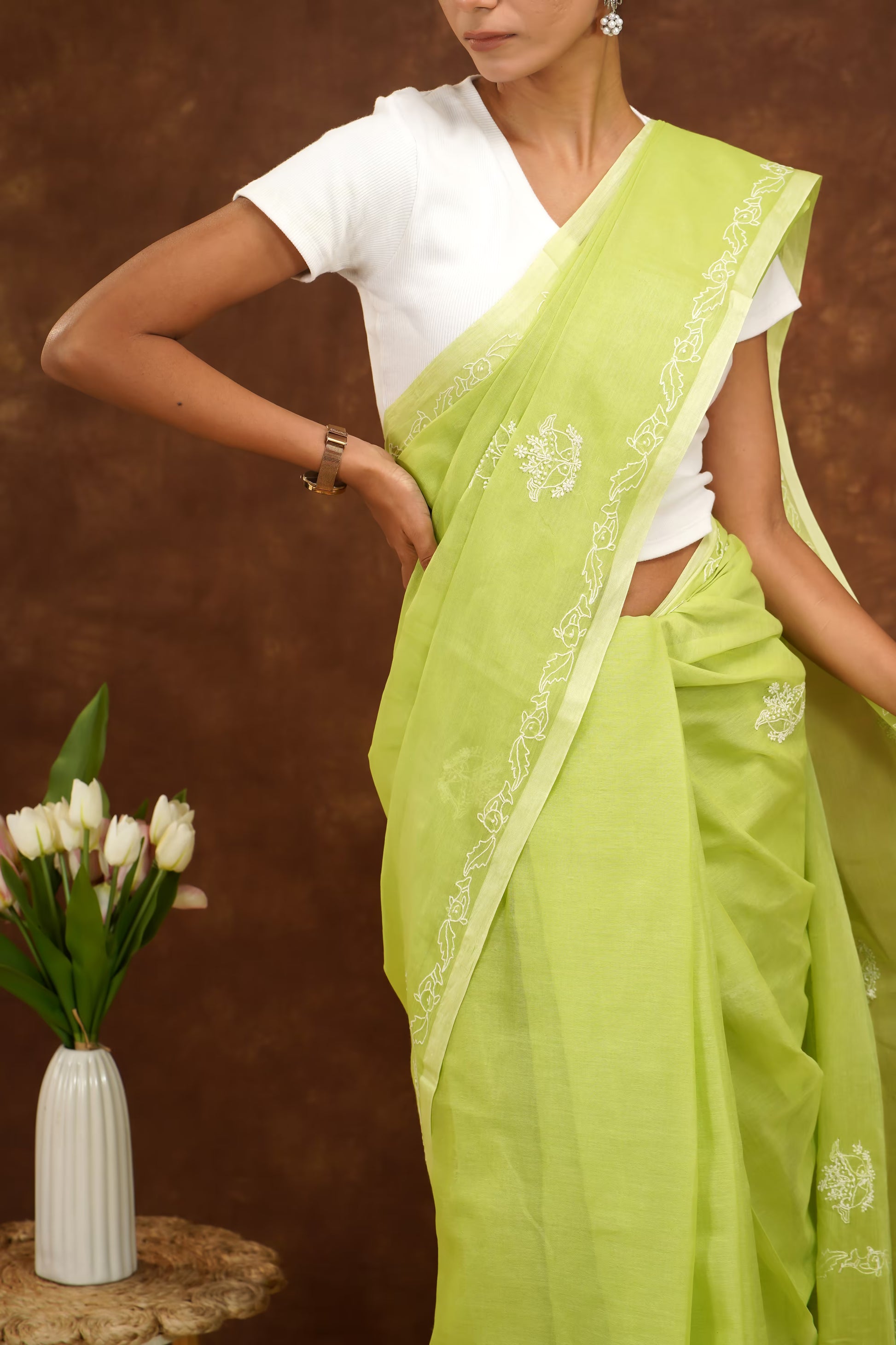 Woman wearing a light green saree with a white blouse against a brown background