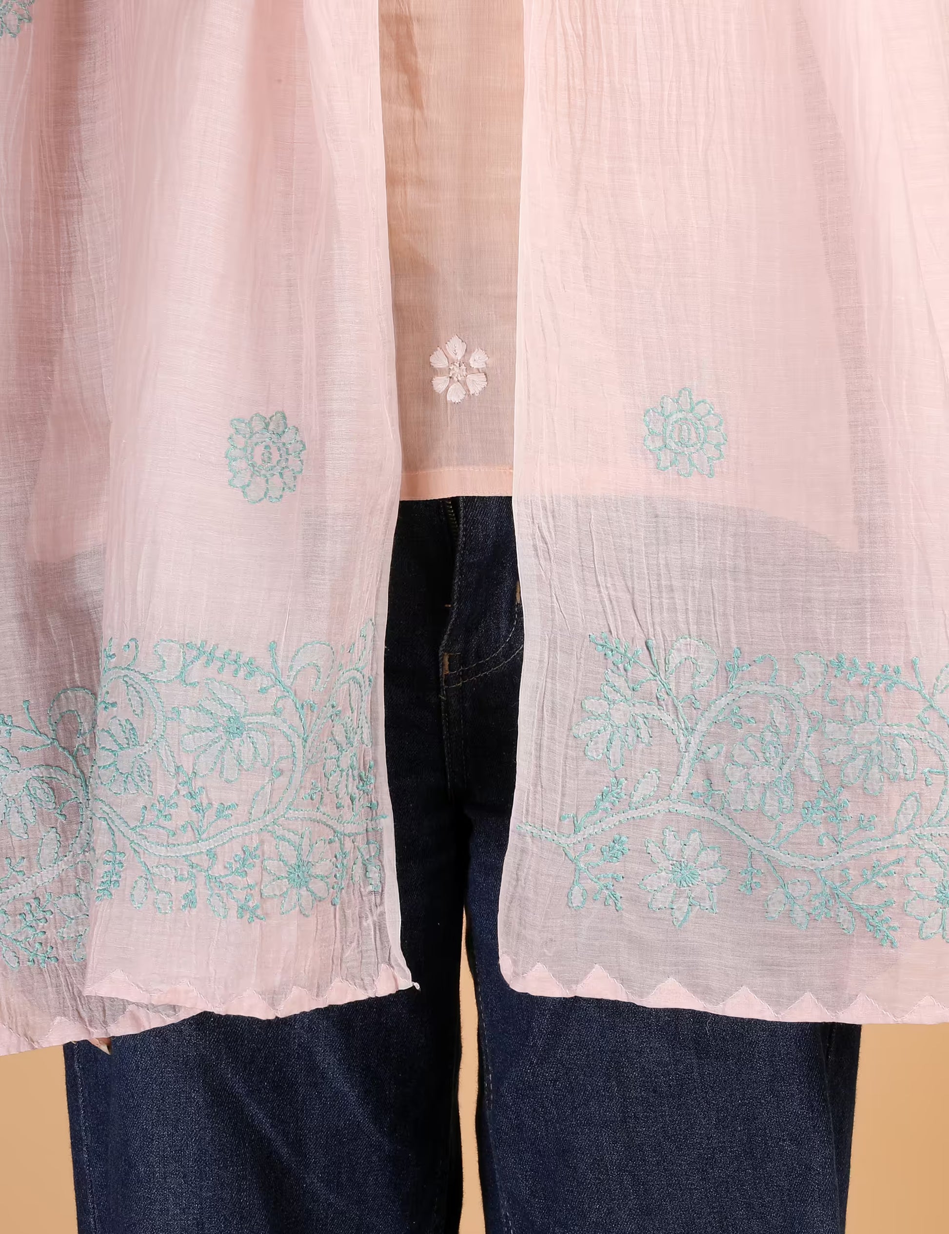 Light pink Hand embroidered  Chikankari fabric with blue patterns over dark jeans on a beige background