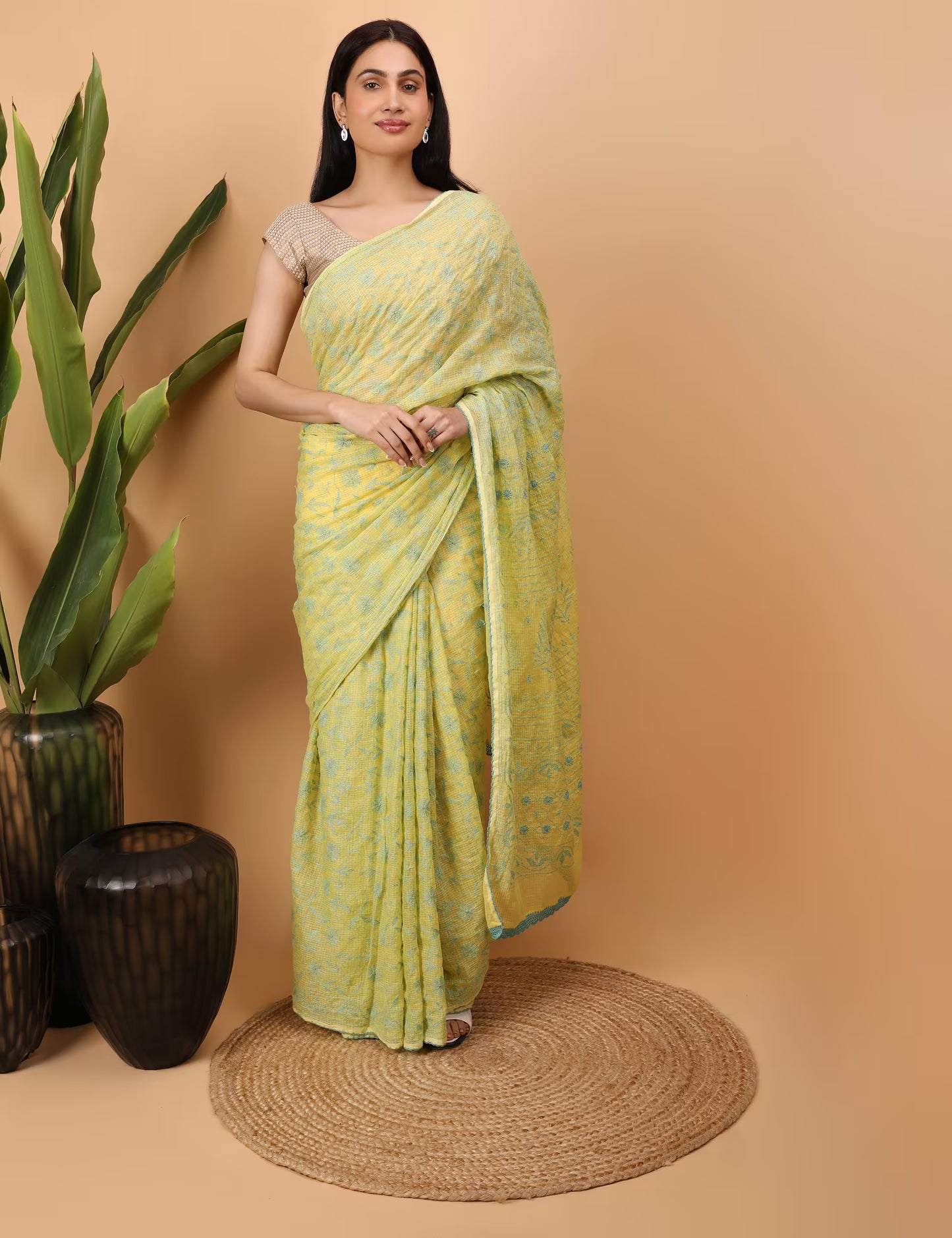 Woman in a yellow  Chikankari saree standing against a beige background with decorative elements.