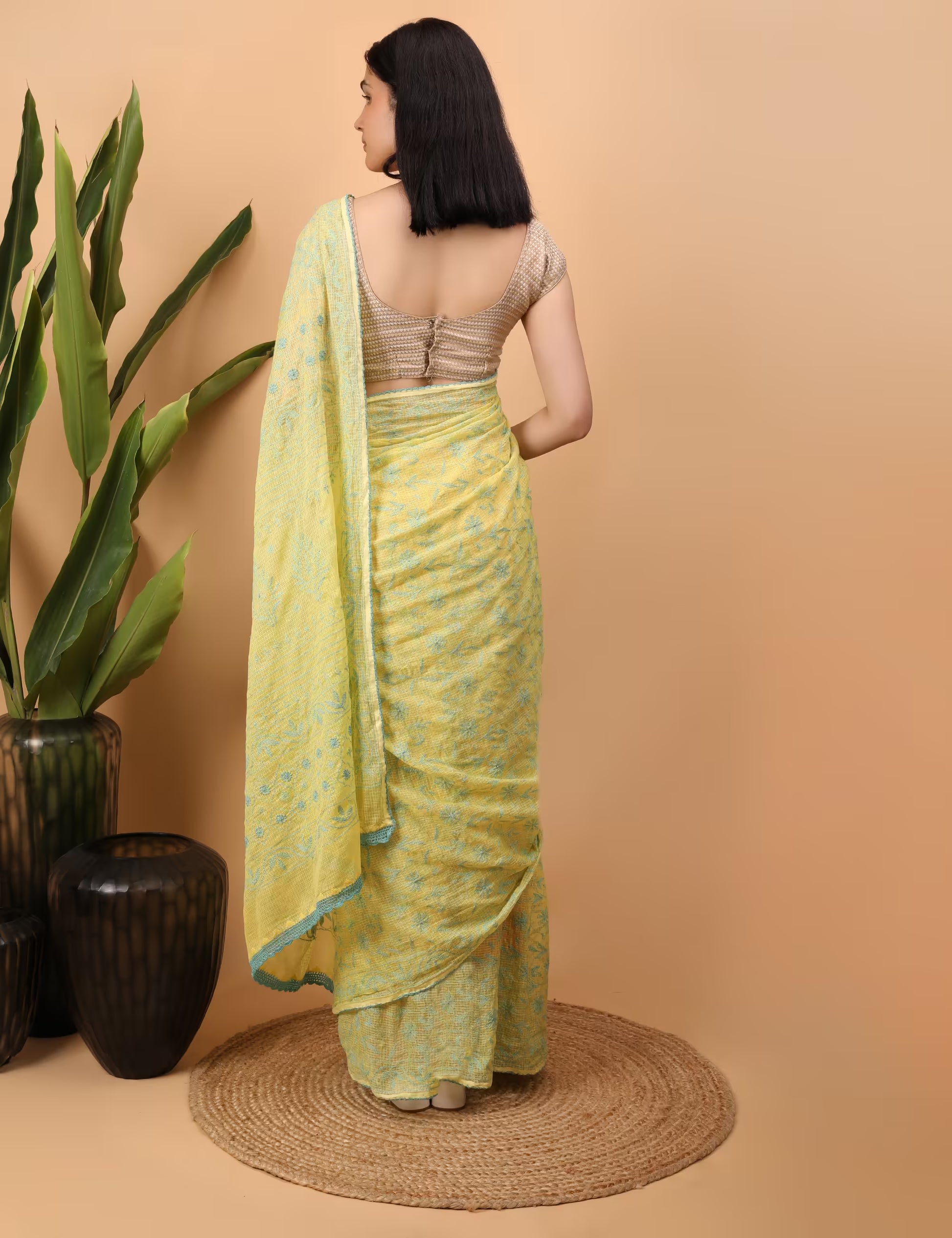 Woman in a yellow saree with Green Chikankari patterns standing against a beige background