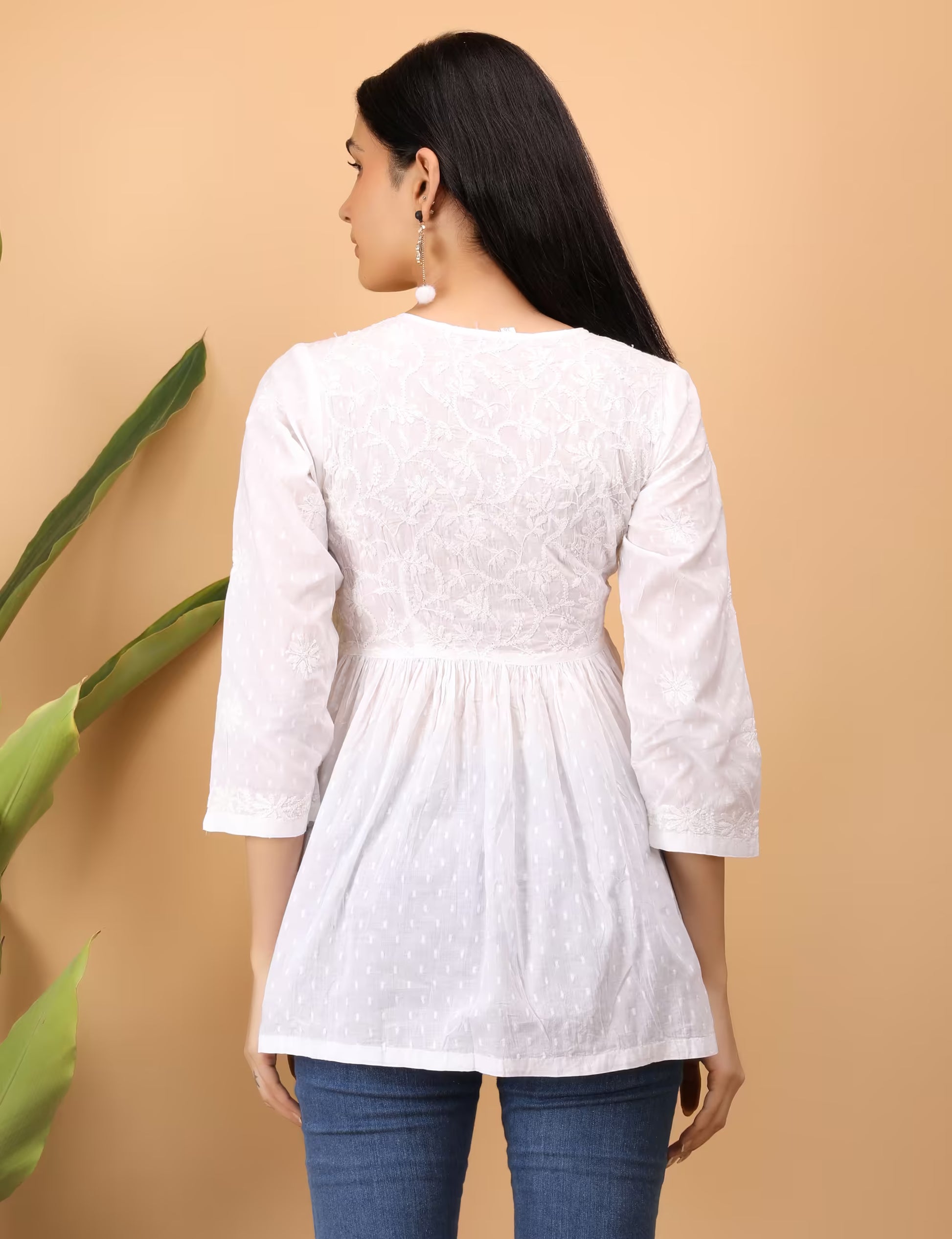 Woman wearing a white embroidered  Chikankari top with blue jeans against a beige background